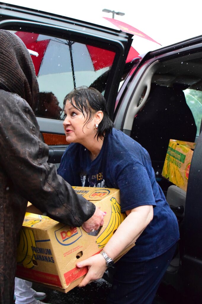 A OneGenAway volunteer loads a food box into an SUV in the rain.