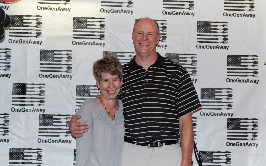 Connie Bond and Mark Bond hug on a red carpet in front of a OneGenAway logo step-and-repeat background